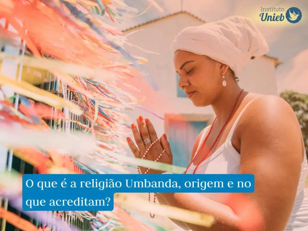 mulher com mãos fechadas em prece com roupa branca e pano branco na cabeça, praticante da Umbanda, de frente para grade com fitas de cetim amarradas, também há uma frase em fundo azul que diz "o que é a religião Umbanda, origem e no que acreditam?" e uma logo acima do Instituto Unieb