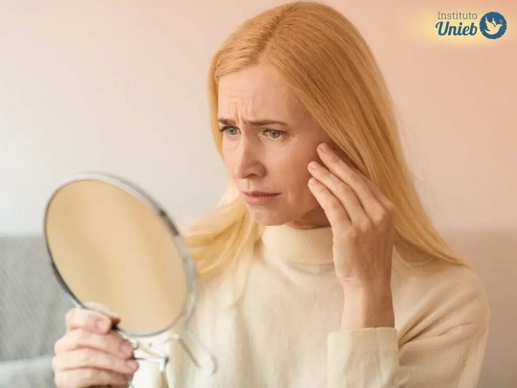 Mulher de cabelo loiro se olhando no espelho com tristeza