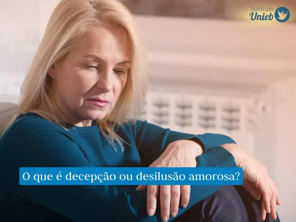O que uma decepção amorosa pode causar? Mulher madura com suéter azul sentada com braços no joelho e expressão de decepção