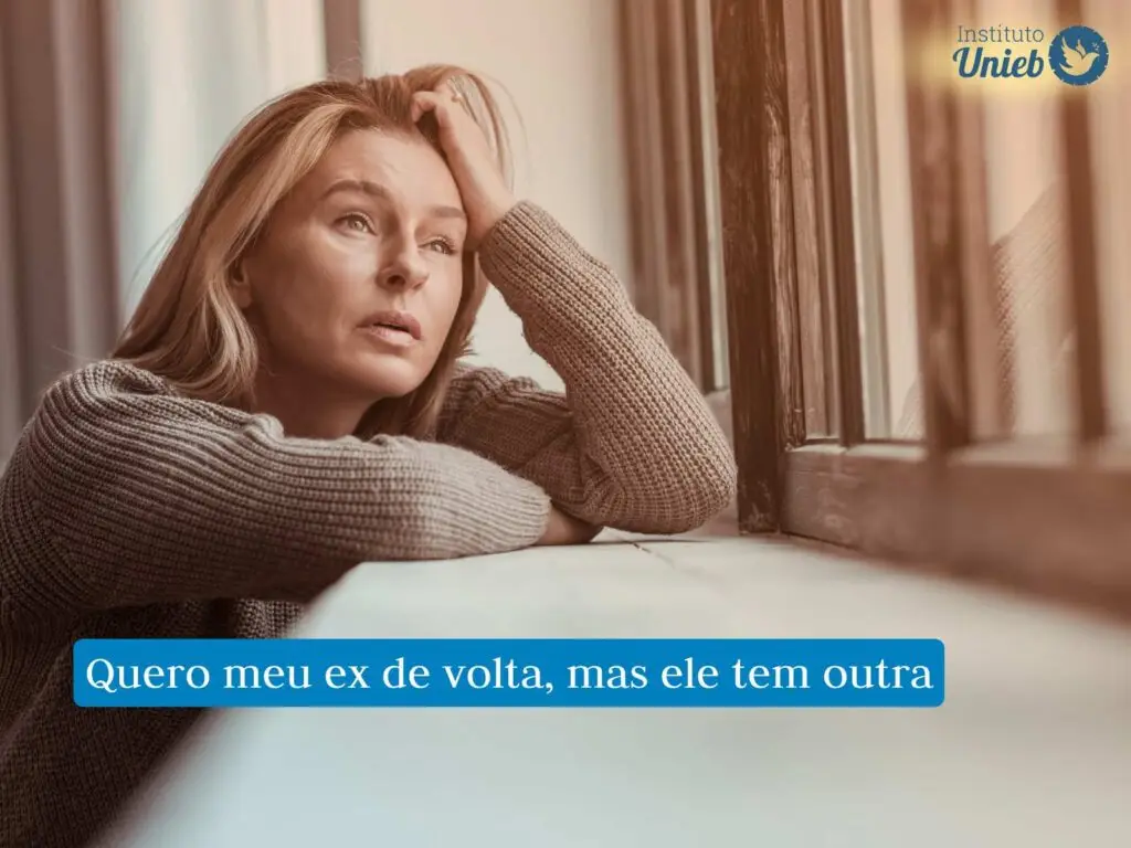 Mulher vestindo suéter com os braços apoiados em uma base e uma mão na cabeça, enquanto olha pela janela com expressão de tristeza