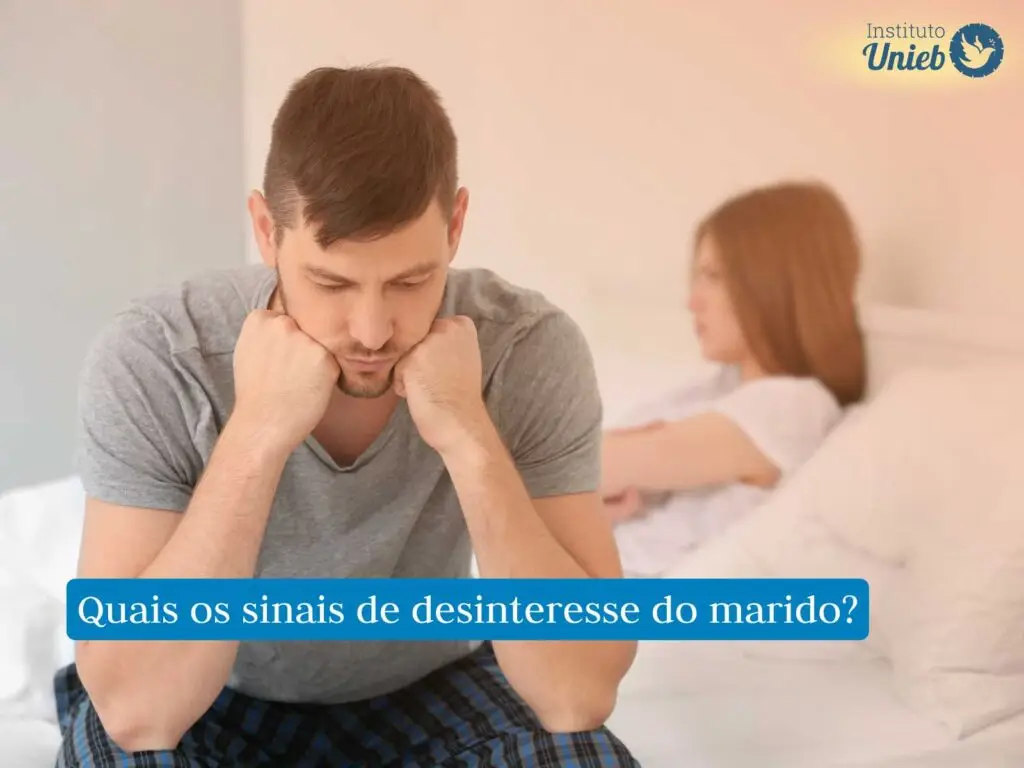 Homem com a cabeça apoiada nos braços pensativo e mulher ao fundo com os braços cruzados