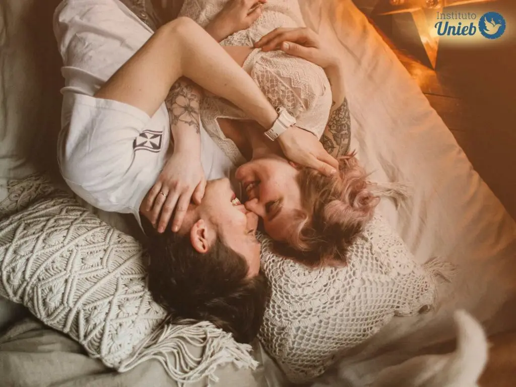 Casal deitado na cama de frente para o outro se abraçando e fazendo gestos de carinho