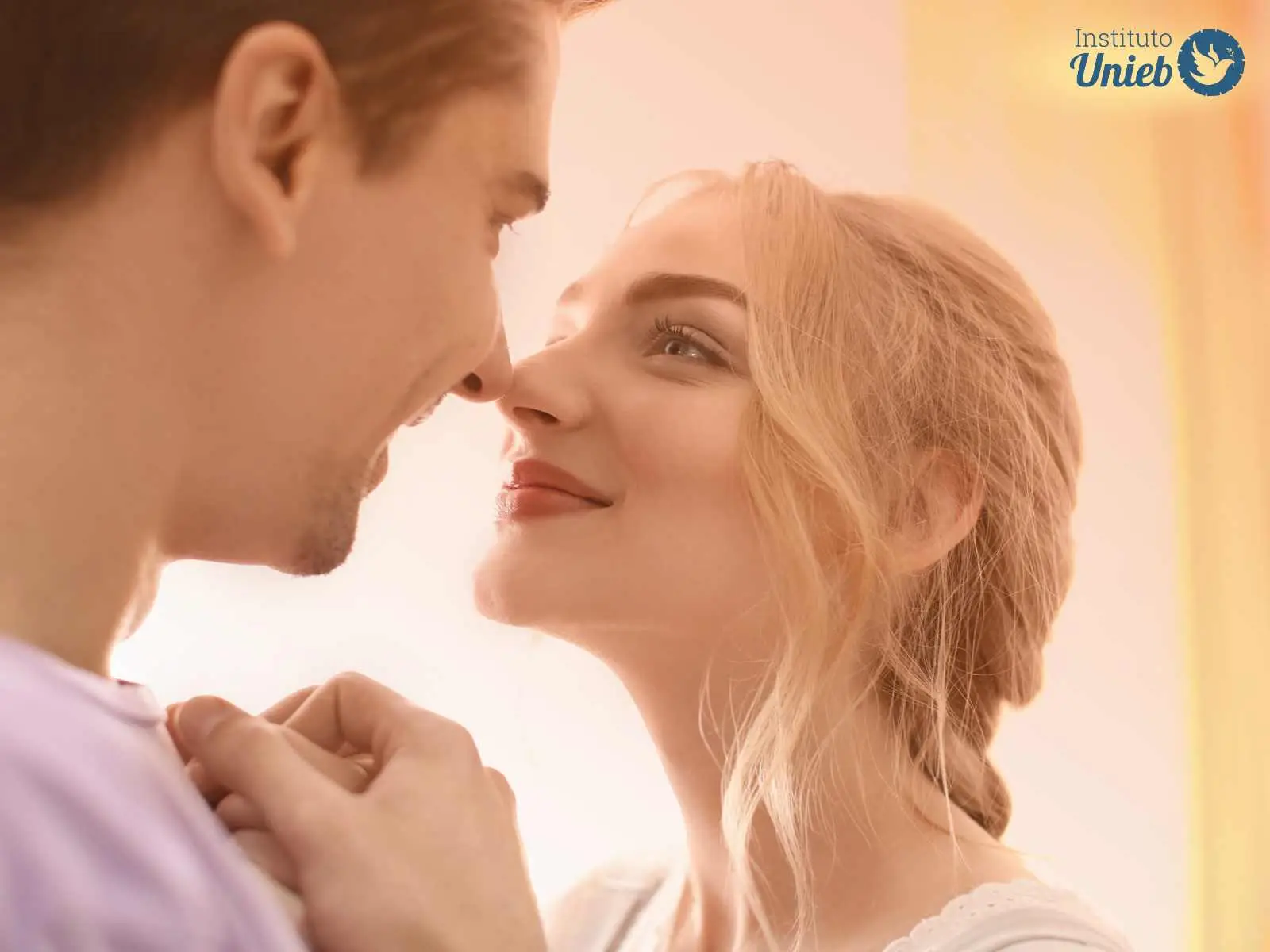 Homem de cabelo castanho e mulher loira com cabelo preso olhando um para o outro de frente