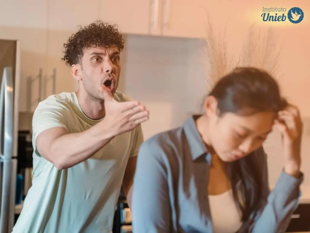 Mulher com cabeça baixa de costas para homem com braço esticado diante de uma briga