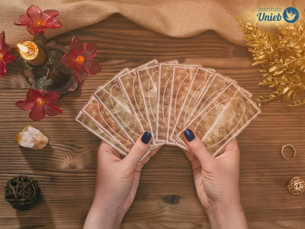 Mãos femininas seguram um baralho de cartas de tarot aberto em cima de mesa de atendimento espiritual