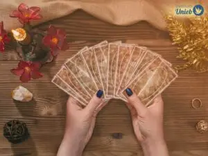 Mãos femininas seguram um baralho de cartas de tarot aberto em cima de mesa de atendimento espiritual