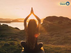Mulher de costas com as mãos levantadas em prece ao ar livre com um pôr-do-sol ao fundo