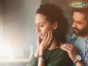 Blog Mulher com mãos no rosto e expressão chateada, enquanto homem segura seu ombro tentando se desculpar