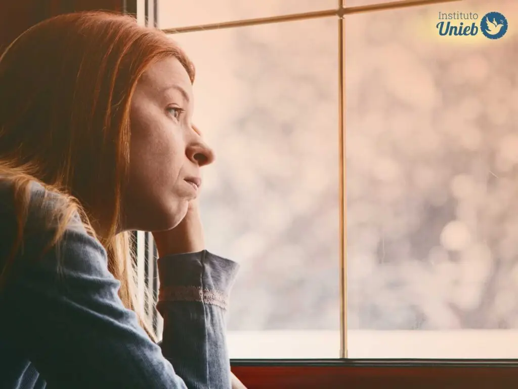 Mulher com expressão triste olhando pela janela
