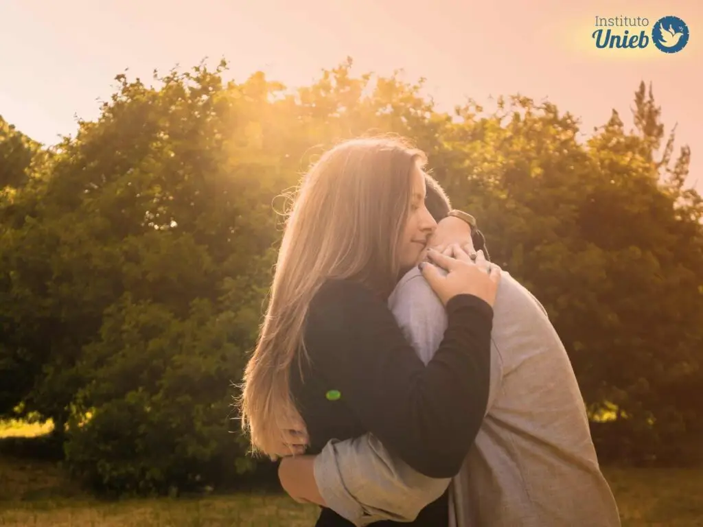 Casal de homem e mulher se abraçando com raios de sol brilhando no horizonte