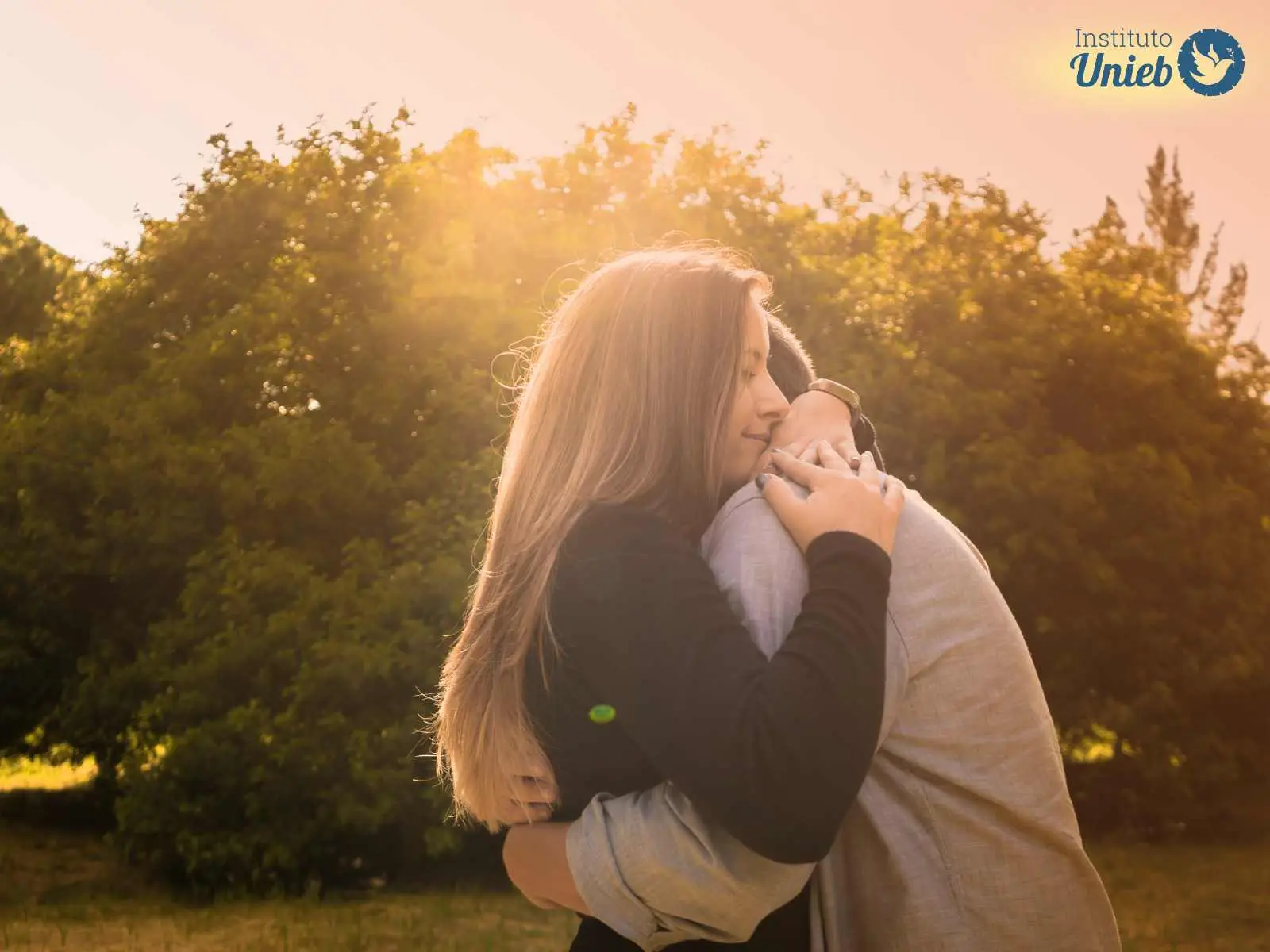 Casal de homem e mulher se abraçando com raios de sol brilhando no horizonte