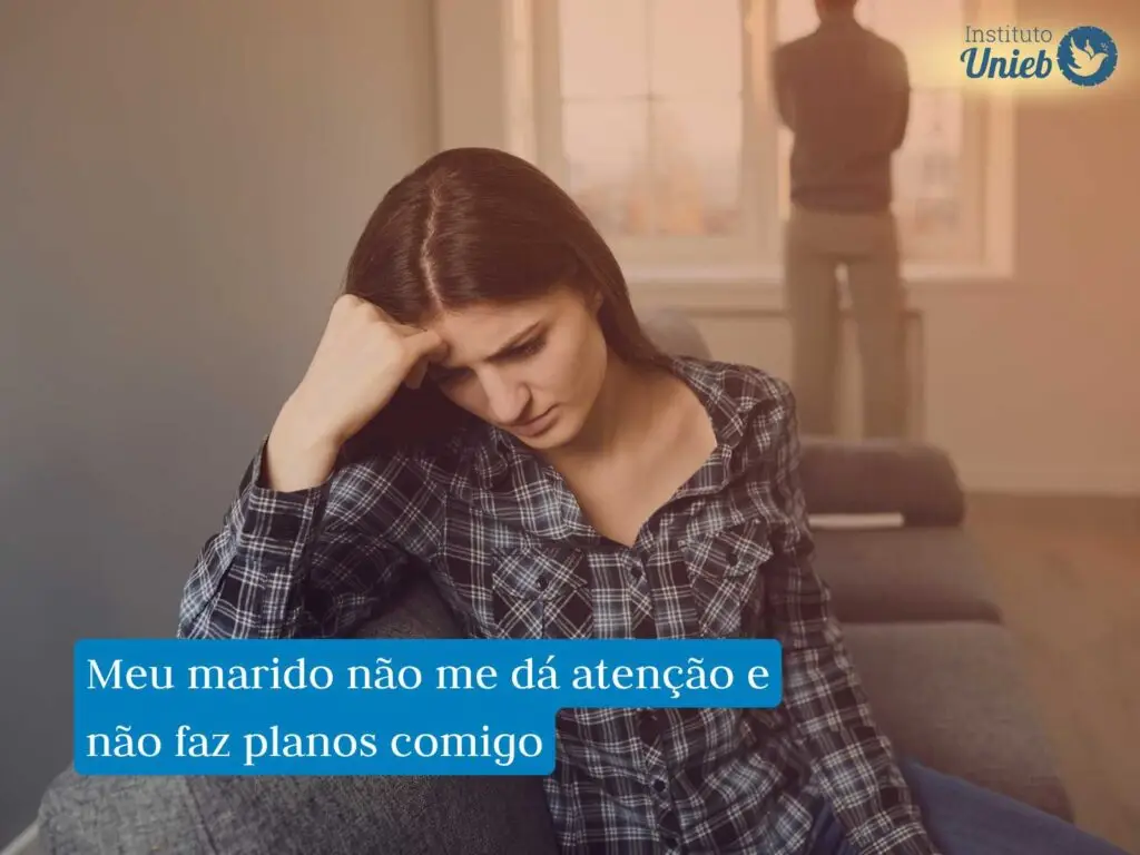 Mulher com a cabeça apoiada no braço e expressão triste com homem ao fundo de costas olhando pela janela