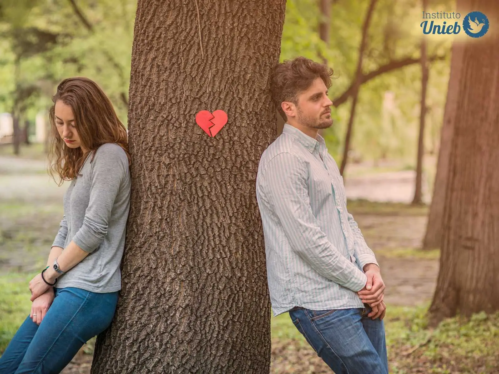 Homem e mulher em pé encostados um de costas para o outro em uma árvore com um coração partido ao meio preso nela - Instituto Unieb (Pai de santo Roberson Dariel) - Contato 11 96982-1121 - CEP 14801-040 - Av. Dom Pedro II 562, Centro, Araraquara, SP