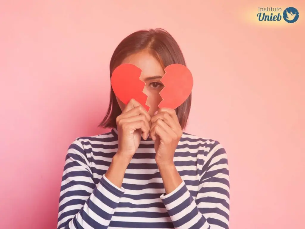 Mulher usando camisa de manga comprida listrada segurando um coração partido na frente do rosto