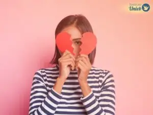 Mulher usando camisa de manga comprida listrada segurando um coração partido na frente do rosto
