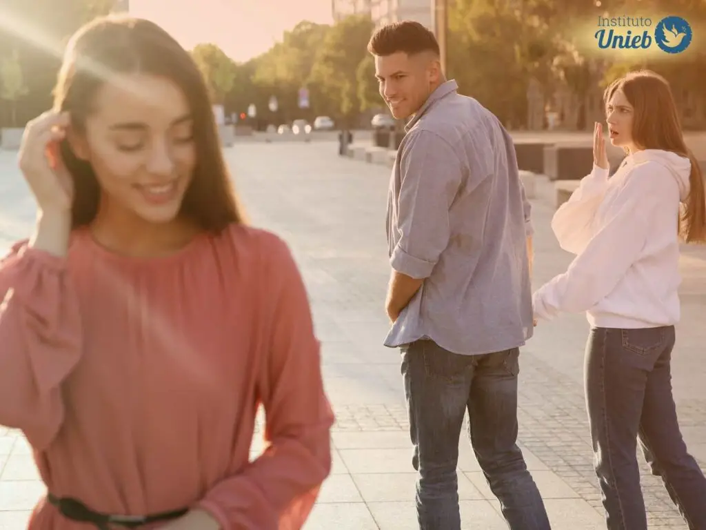 Casal de homem e mulher passam por uma mulher na rua e o homem olha para trás para ela com desejo enquanto ela sorri e ajeita o cabelo