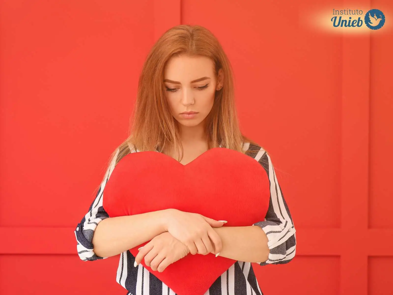 Mulher triste olhando para baixo abraçando um coração vermelho