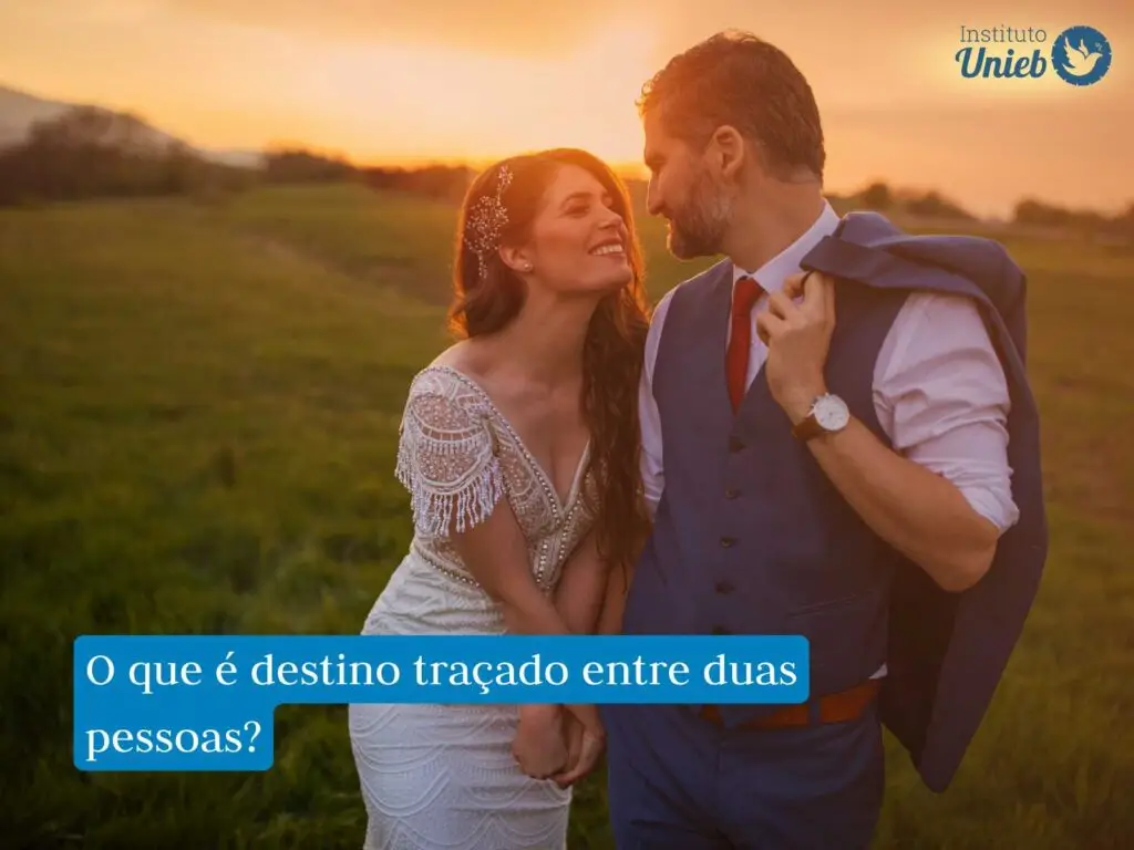 Homem e mulher vestidos de noivos em pose olhando um para o outro em um campo com sol se pondo ao fundo