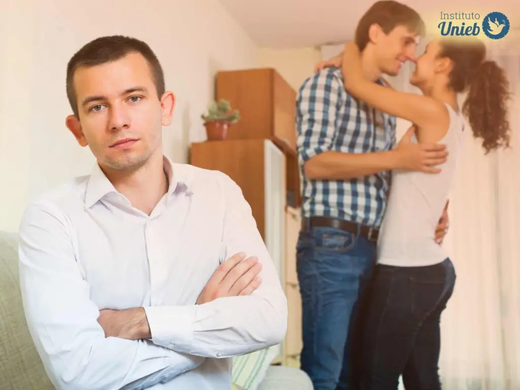 Homem com expressão cansada a frente e ao fundo um casal de homem e mulher se abraçando