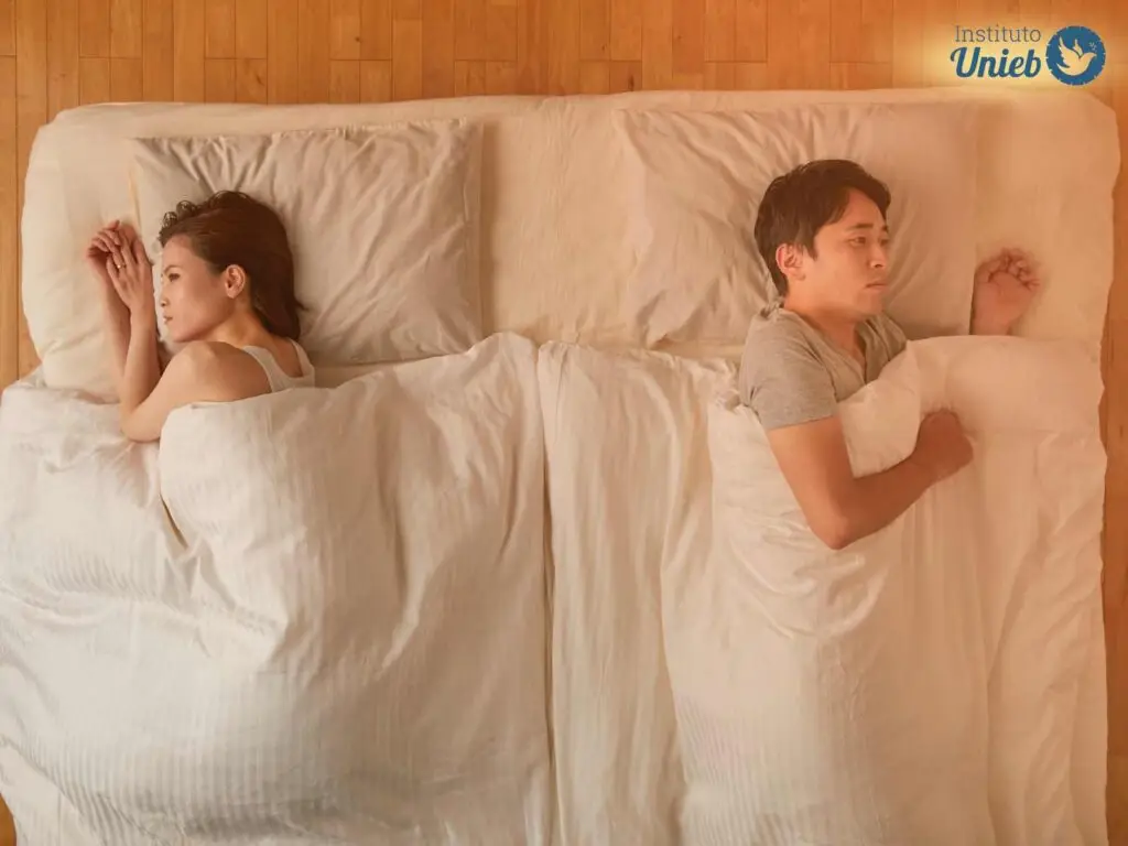 Homem e mulher deitados na cama embaixo de edredom branco de costas um para o outro