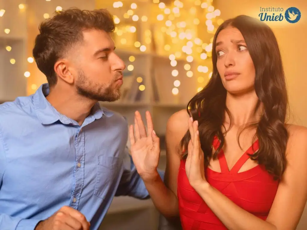 Homem tentando beijar mulher enquanto ela se esquiva e o afasta com as mãos