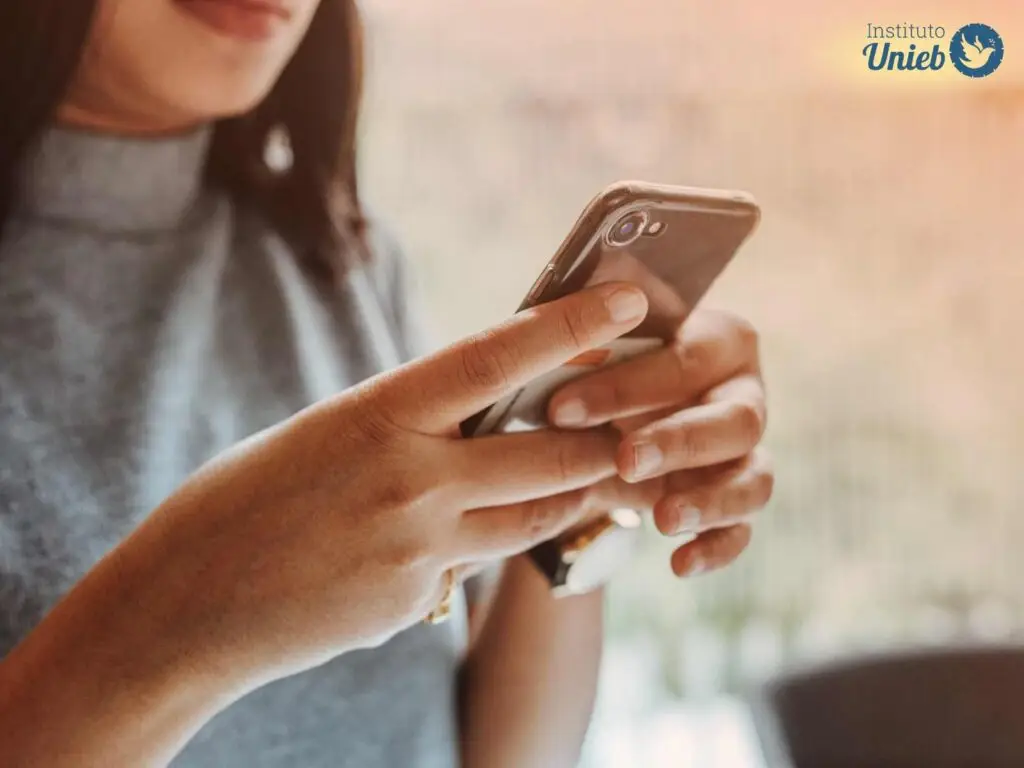 Mulher vestindo blusa cinza com celular na mão mandando mensagem