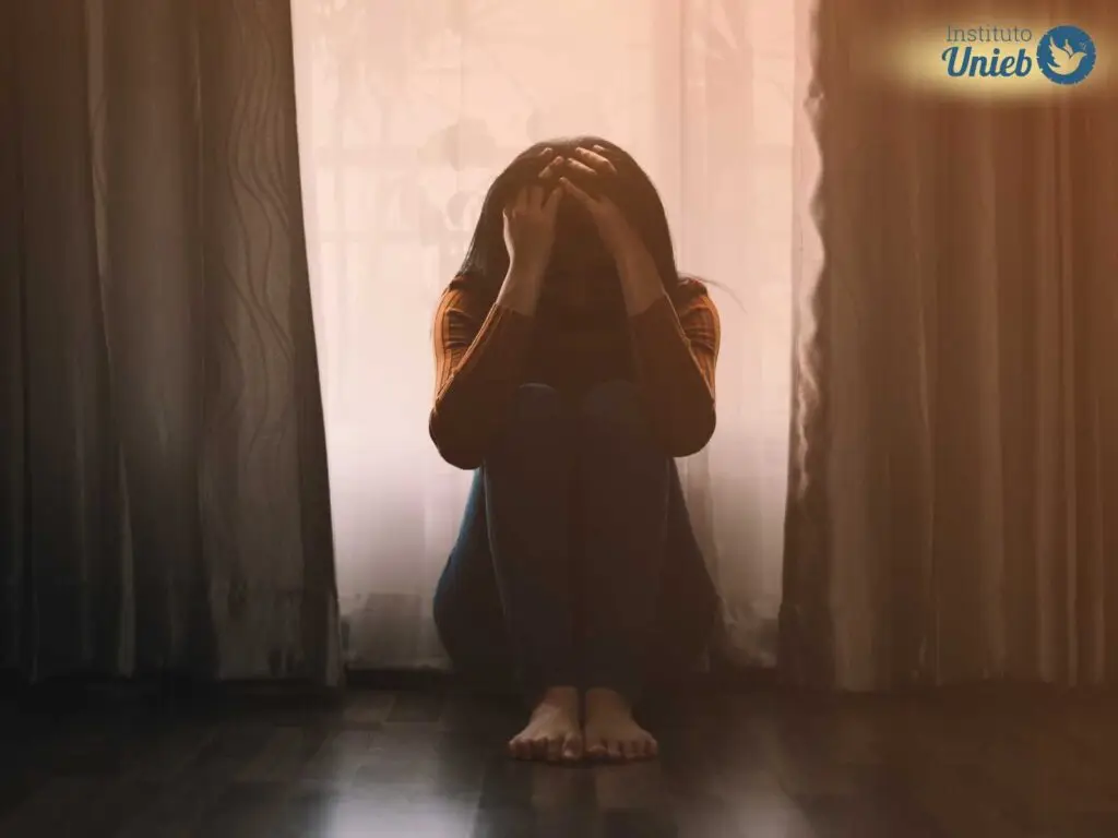 Mulher sentada no chão do quarto com as mãos na cabeça