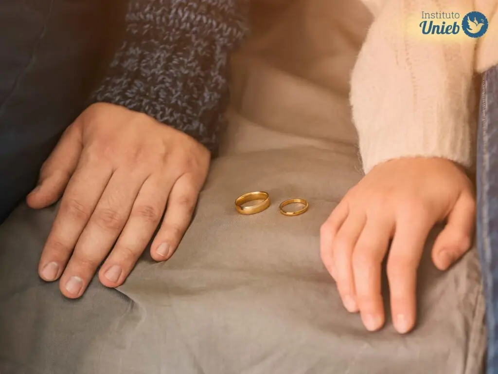 Casal sentado um ao lado do outro com alianças no sofá entre eles