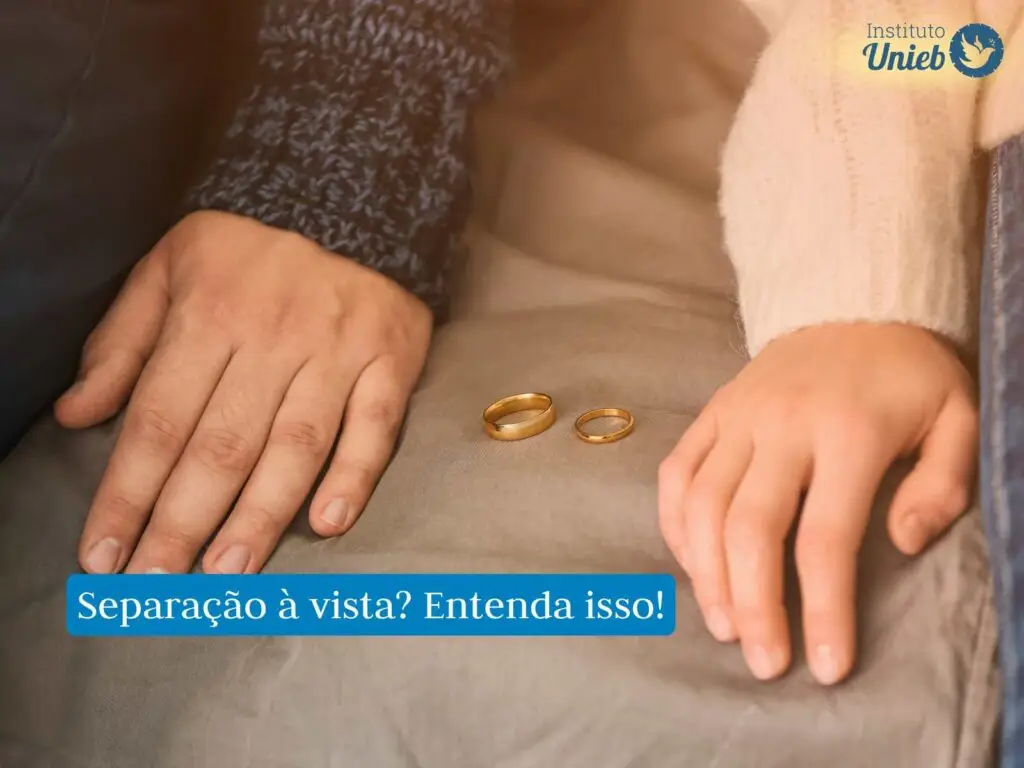 Casal sentado um ao lado do outro com alianças no sofá entre eles