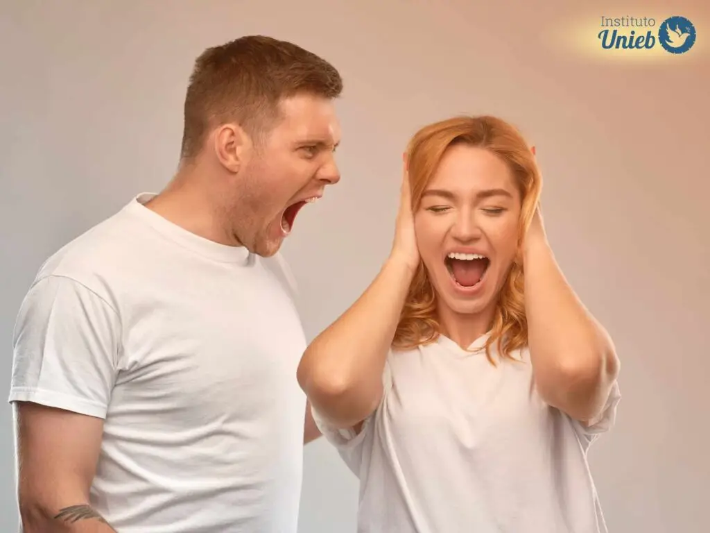 Homem vestindo camiseta branca gritando com mulher que também está de camiseta branca com as mãos tapando o ouvido e gritando