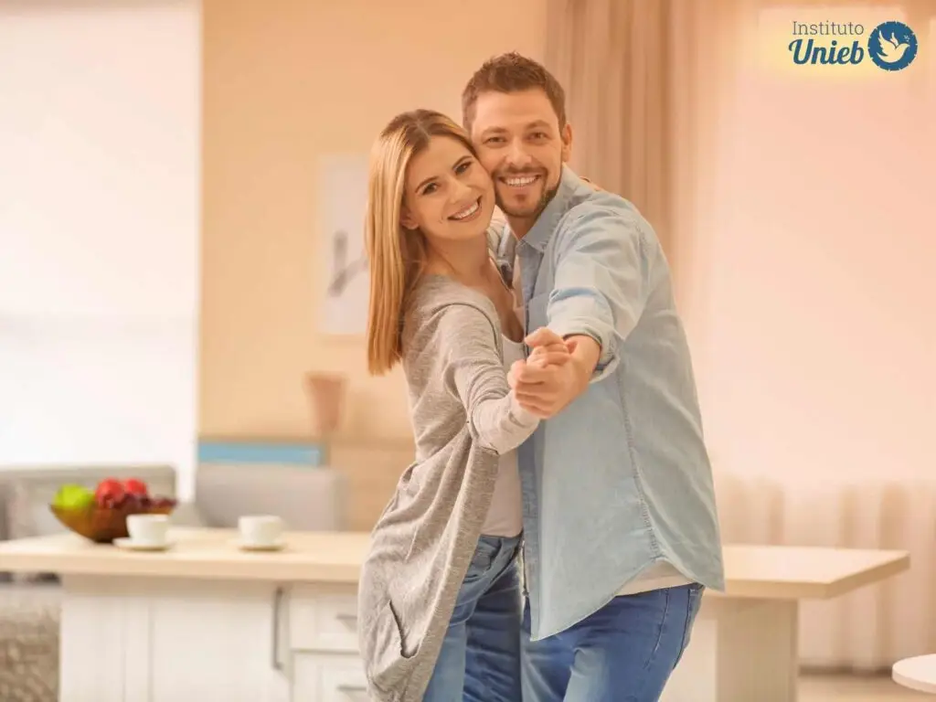 Homem e mulher abraçados e de mãos dadas dançando dentro da casa