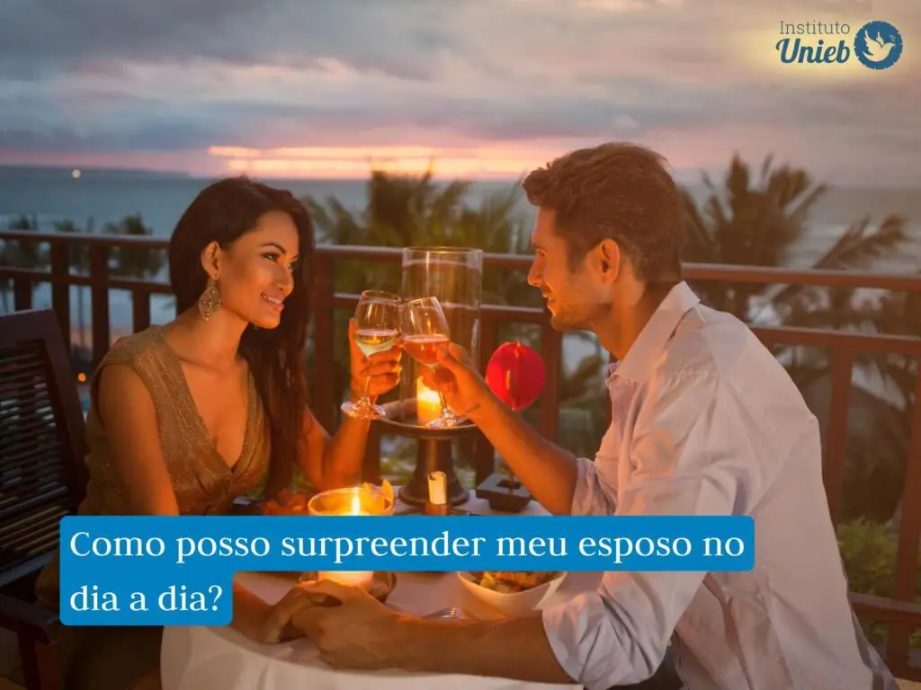 Homem e mulher sentados a mesa em jantar a luz de velas com taças nas mãos brindando e pôr do sol ao fundo