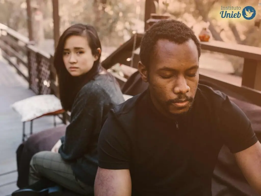 Homem e mulher sentados em banco ao ar livre de costas um para o outro