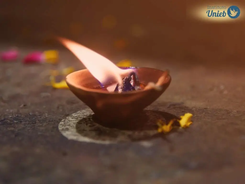 Vela queimando em porta-velas no chão com algumas flores caídas