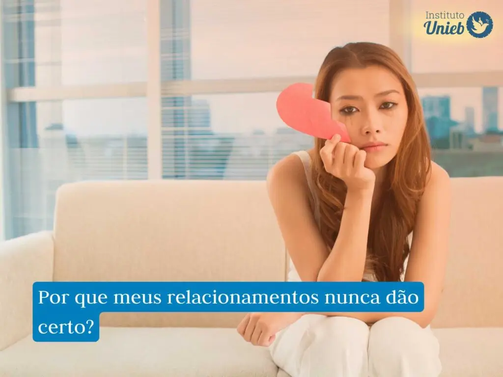 Mulher sentada em sofá com metade de um coração de papel na mão e com o rosto borrado de maquiagem após chorar