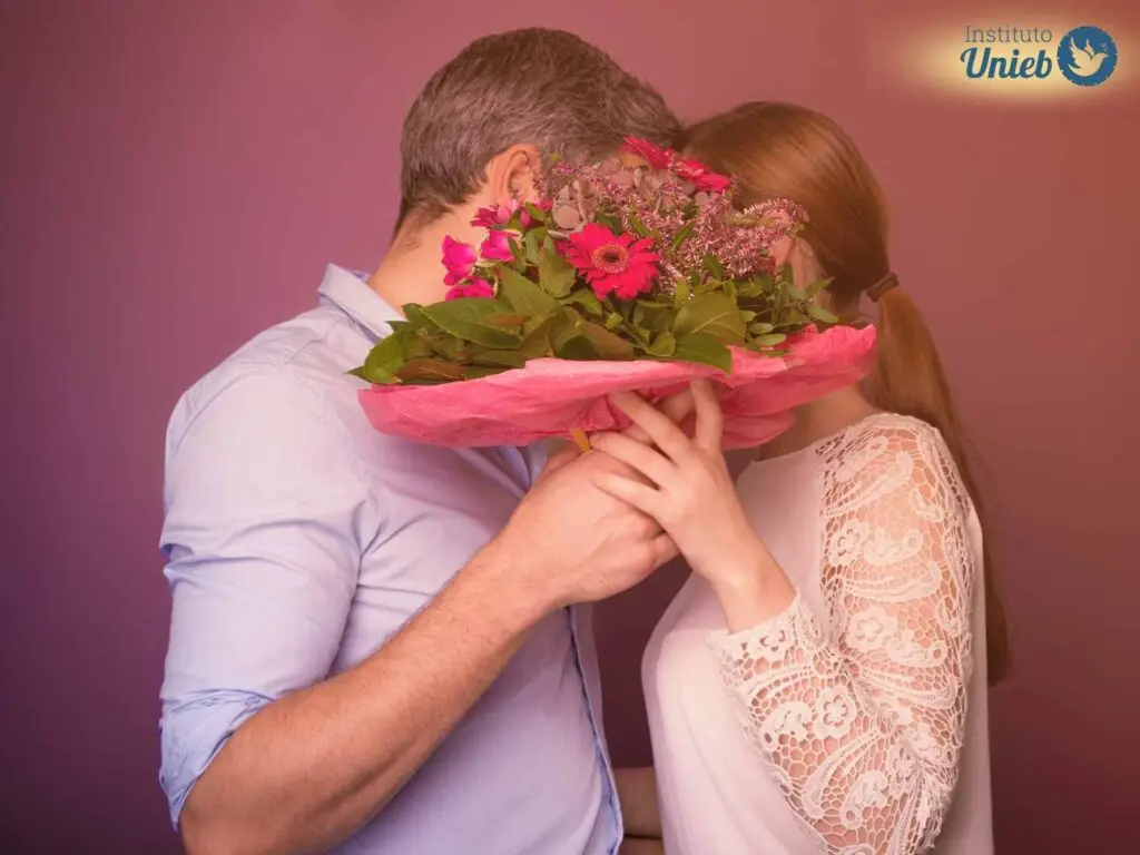 Homem e mulher se beijando com um buquê de flores tampando os rostos
