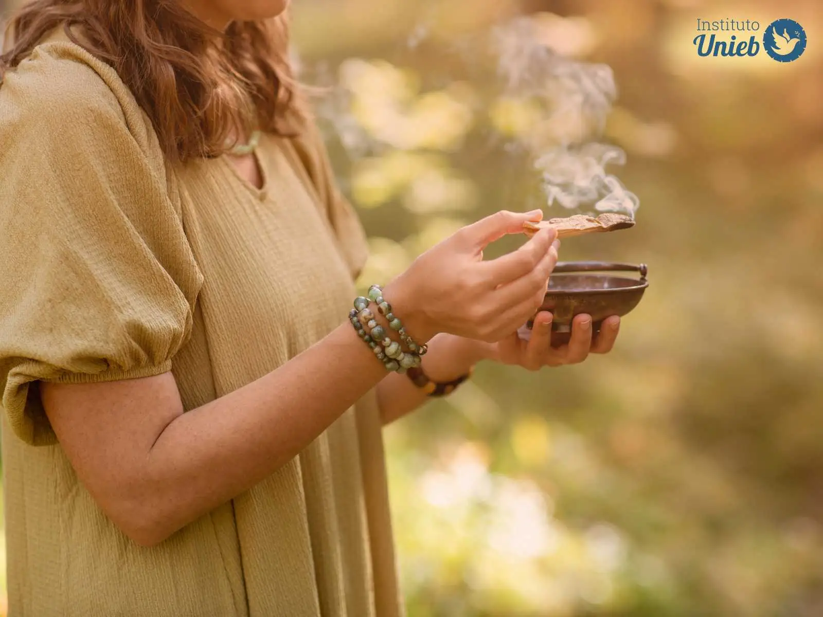 Mulher vestindo camiseta verde musgo segurando uma tigela em uma mão e um defumador em outra praticando um ritual de defumação - Instituto Unieb (Pai de santo Roberson Dariel) - Contato 11 96982-1121 - CEP 14801-040 - Av. Dom Pedro II 562, Centro, Araraquara, SP