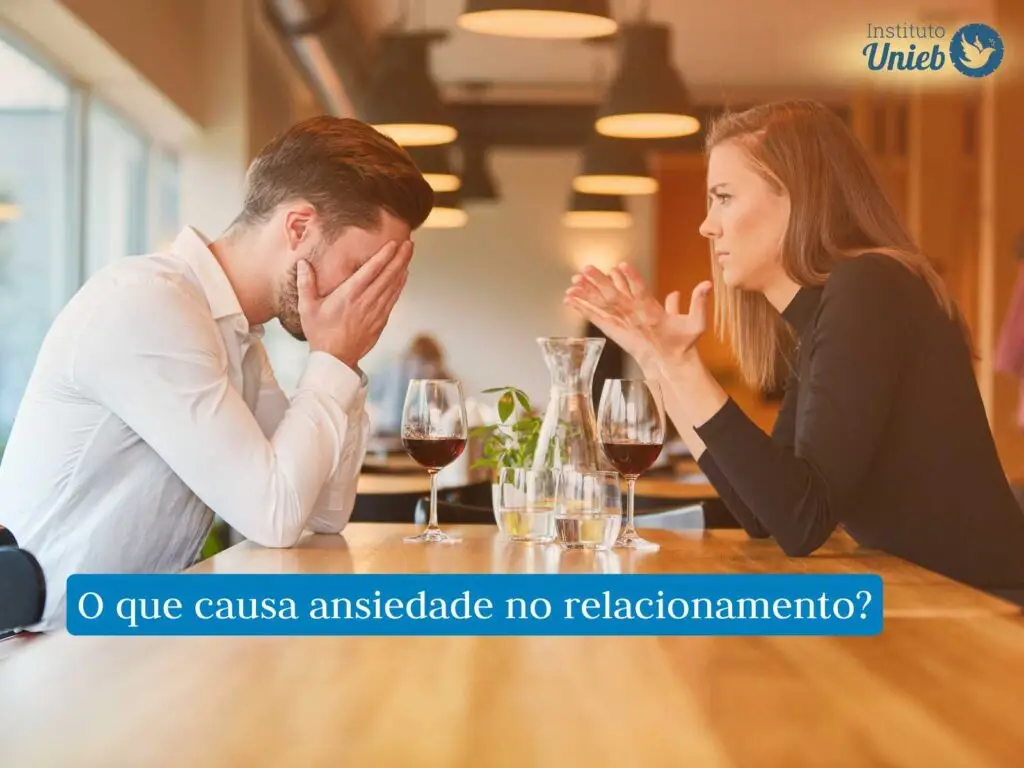 Homem e mulher sentados com braços apoiados em mesa de madeira com taças de vinho e com gestos de discussão