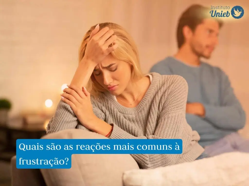 Casal de homem e mulher sentados no sofá, onde homem veste camiseta azul e está de braços cruzados e mulher com blusa cinza está com a cabeça apoiada na mão