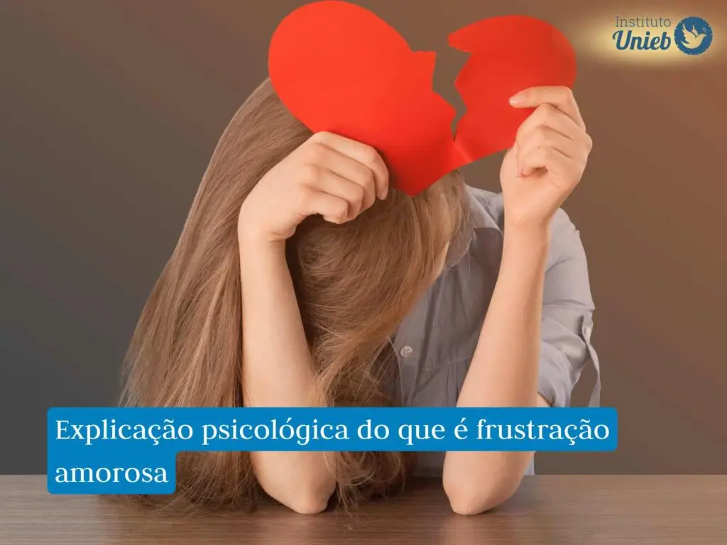 Mulher com a cabeça abaixada e cotovelos apoiados na mesa segurando um coração vermelho partido ao meio