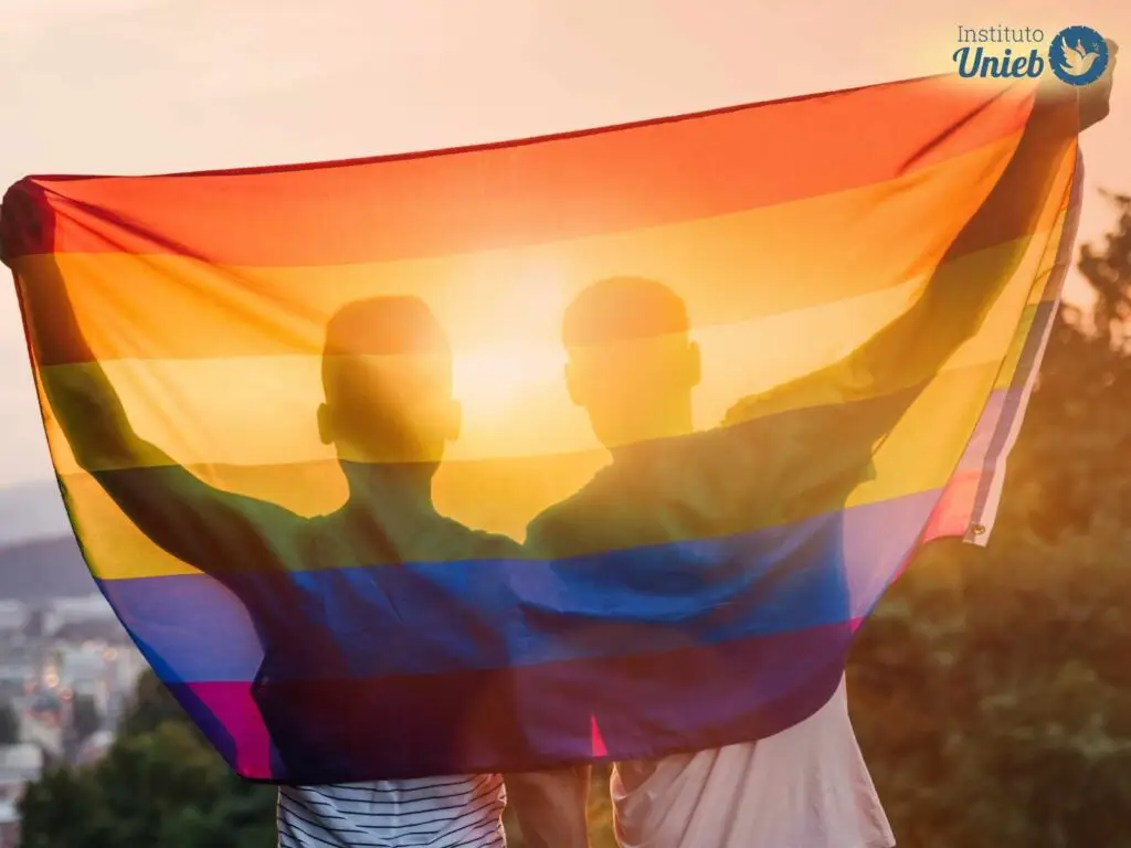 Dois homens abraçados de costas com uma bandeira arco-íris que simboliza a comunidade LGBT