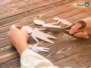 Mãos usando uma tesoura para cortar uma família de papel em cima de uma mesa de madeira