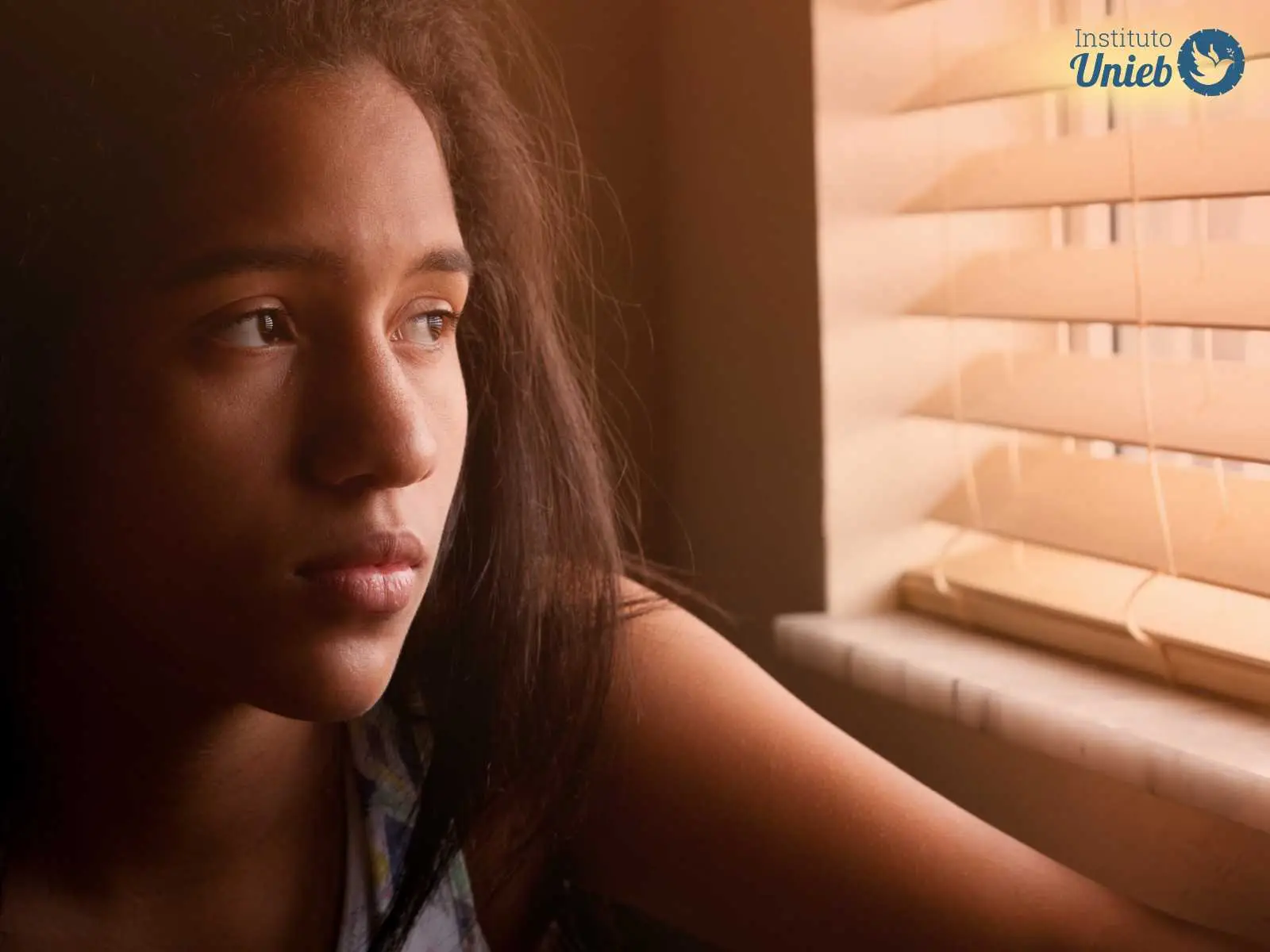 Rosto de uma mulher próximo à câmera olhando pela persiana da janela