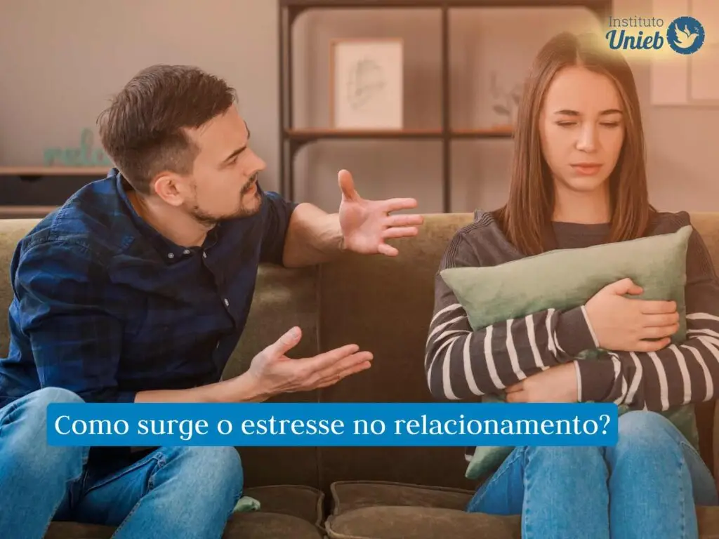 Casal de homem e mulher sentado no sofá, onde mulher está segurando uma almofada próxima ao corpo e homem está gesticulando enquanto briga com sua parceira