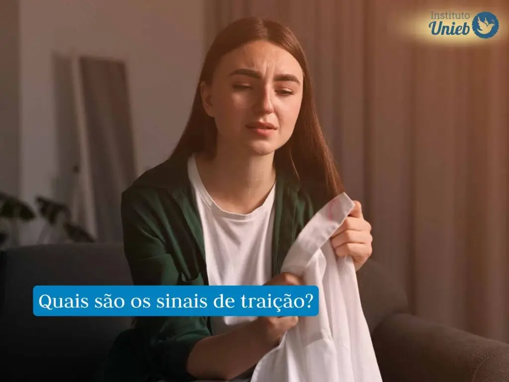 Mulher jovem segurando camisa masculina branca com marca de batom na gola com expressão de tristeza