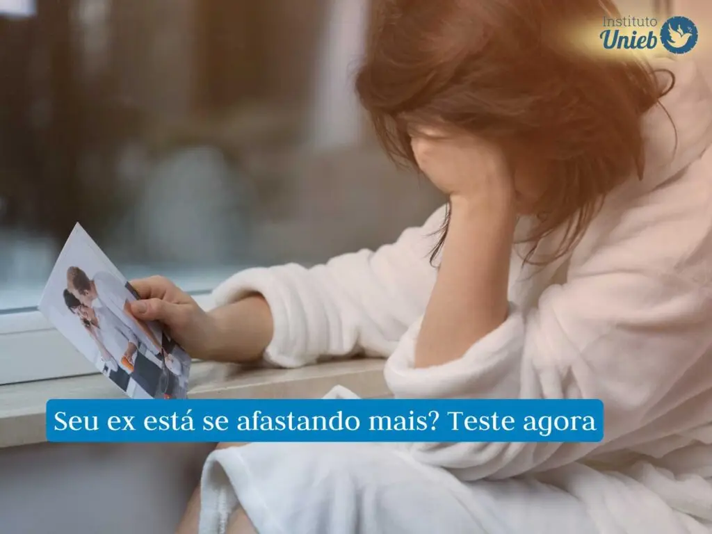 Mulher vestindo roupão branco sentada próximo à janela com fotografia de casal na mão e outra secando lágrimas no rosto