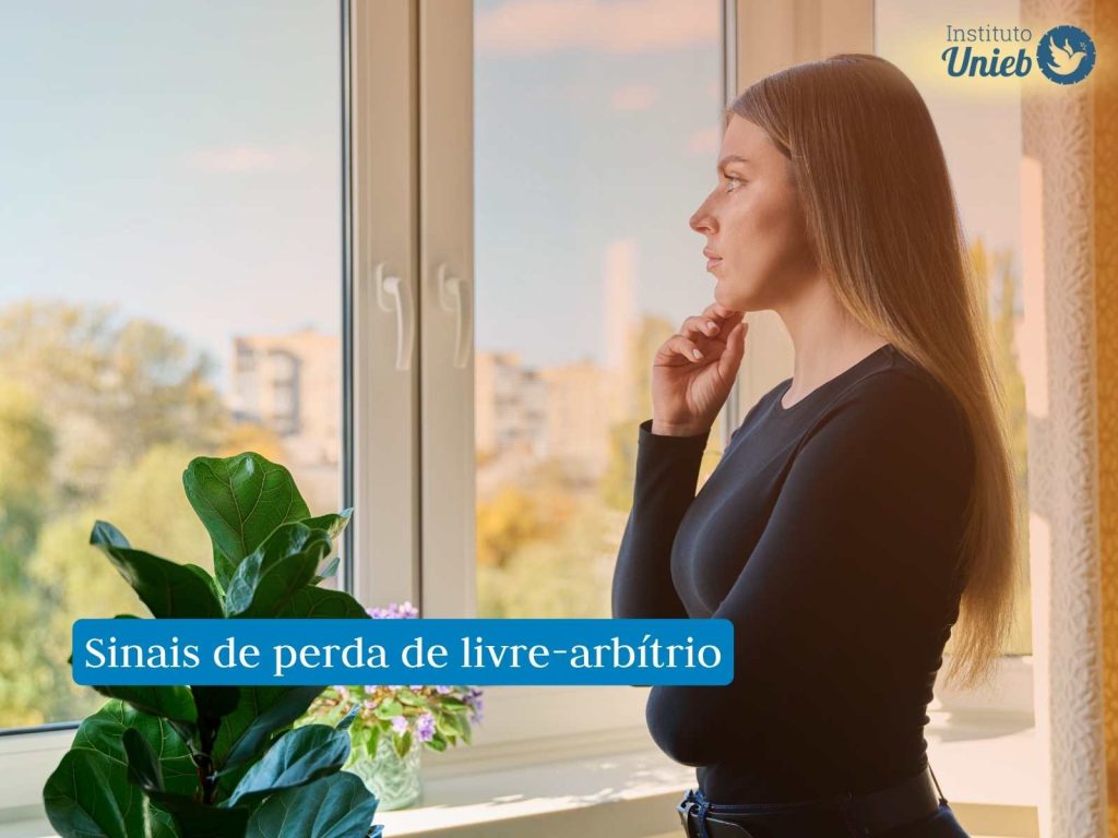 Mulher pensativa observando pela janela representando uma alguém que mostra sinais de perda de livre arbítrio