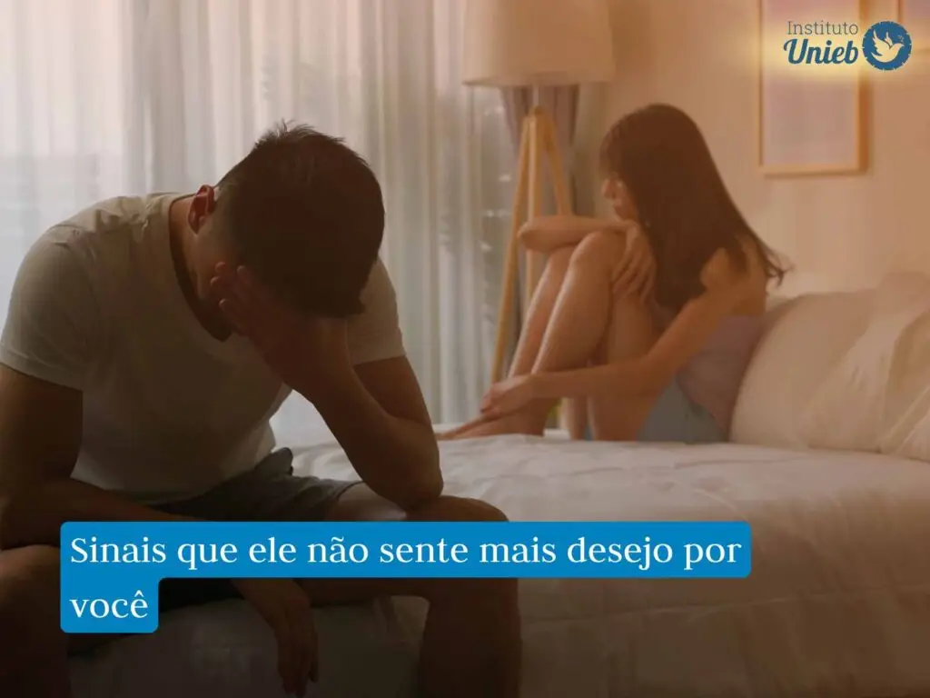 Homem sentado na parte debaixo da cama com a cabeça apoiada na mão e mulher ao fundo sentada na parte superior da cama envolvendo as pernas com os braços