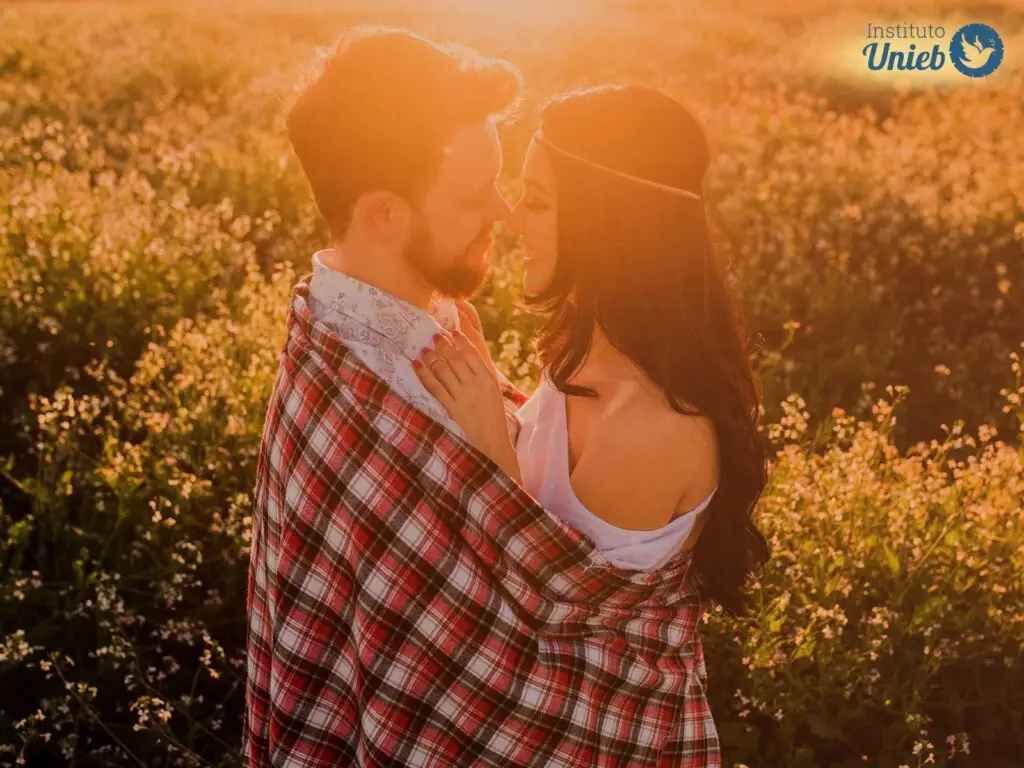 Casal de homem e mulher abraçados olhando de nos olhos um do outro em um local aberto com flores no terreno e raios de sol indicando um entardecer - Instituto Unieb (Pai de santo Roberson Dariel) - Contato 11 96982-1121 - CEP 14801-040 - Av. Dom Pedro II 562, Centro, Araraquara, SP
