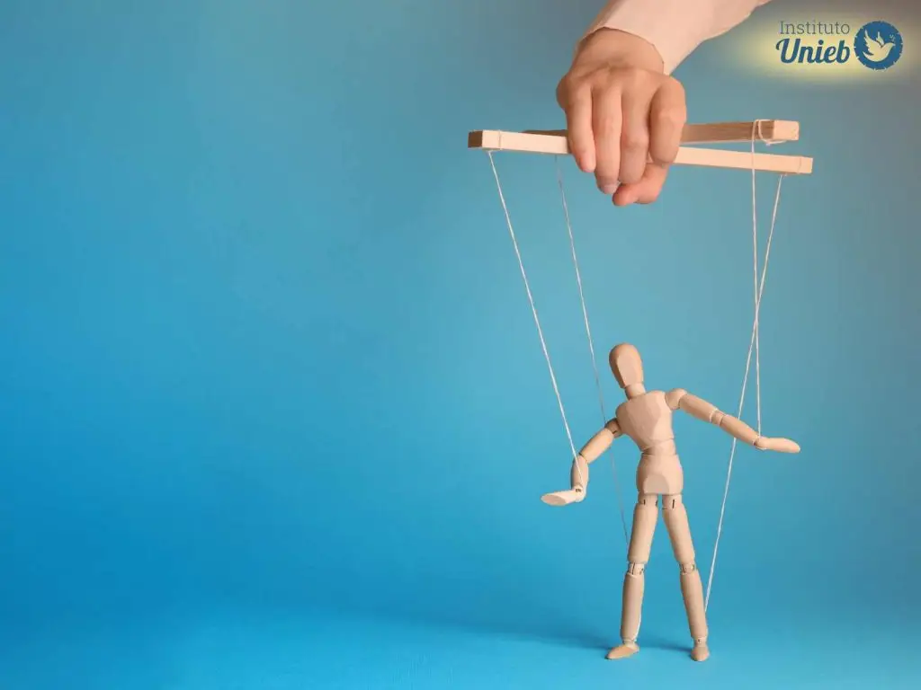 Pequeno boneco de madeira do tipo marionete preso por cordas a uma base de madeira que é segurada por uma mão no alto